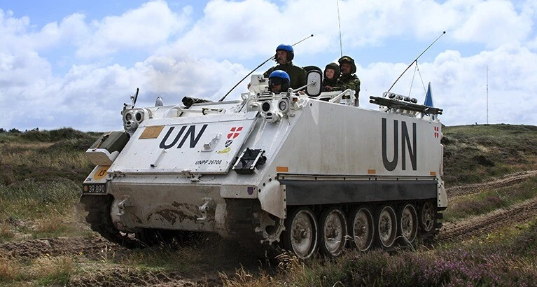 A fully manned UN armored personnel carrier driving full throttle into the training ground.