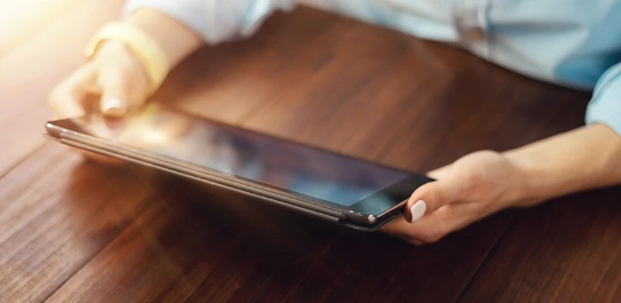 Close up photo of female hands with a digital tablet on wooden table.