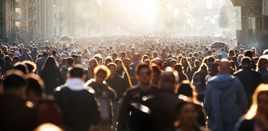 Blurred crowd of thousands of people walking through a wide street.