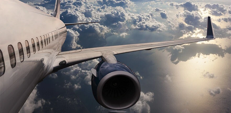 View down the side of an aircraft while flying in the sky, scattered clouds in the distance.