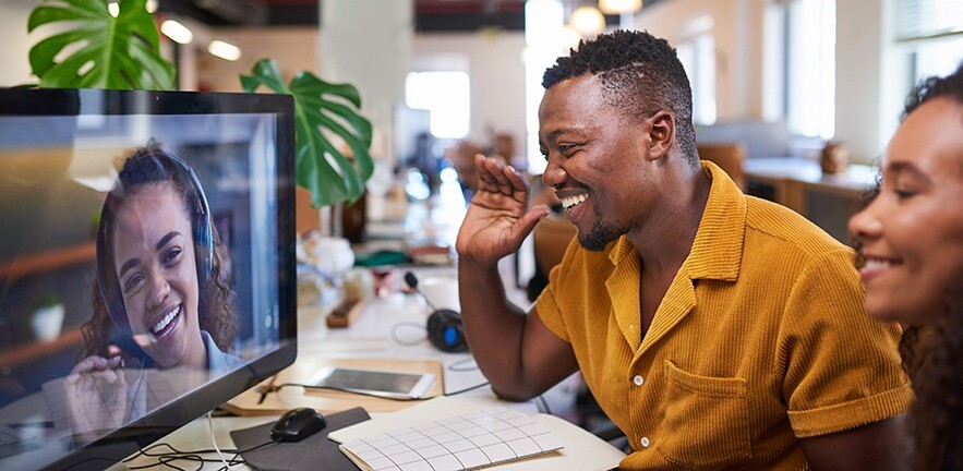 Man waving to his colleague on a video call from his office.