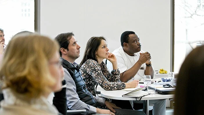 Woman and two men sat around a table in a classroom, listening intently.