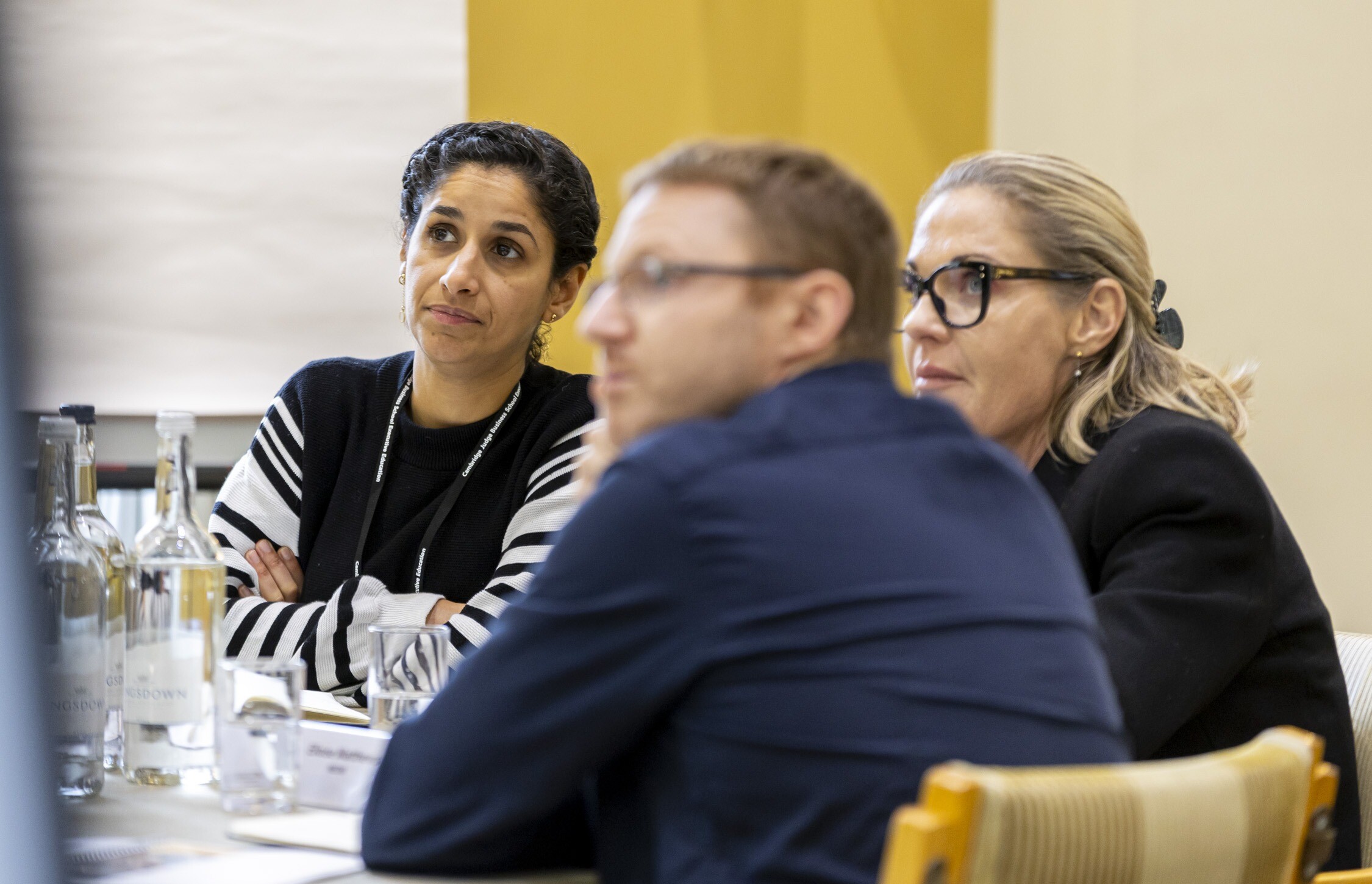 Two women and a man listening in a classroom setting.