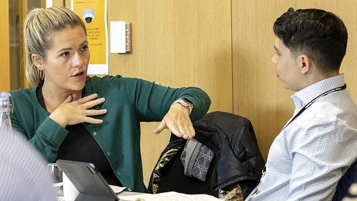 A woman and a man engaging in conversation in a classroom.