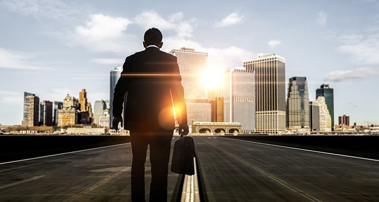 Businessman walking towards skyscrapers.